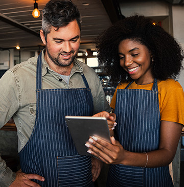 Small business owners wearing aprons smiling at a notepad